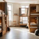 هاستل چیست؟ حریم خصوصی و امکانات مشترک را چگونه مدیریت کنیم؟ تصویر شاخص: نمای مفهومی اتاق اشتراکی هاستل با تختهای جدا و کمدهای شخصی، بدون حضور مهمانان.